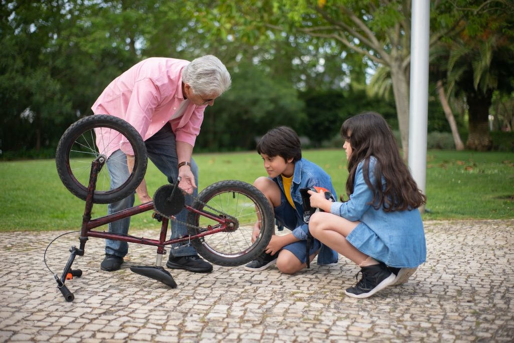 Fotografija dedka, ki popravlja kolo in dva vnuka, ki ga opazujeta
