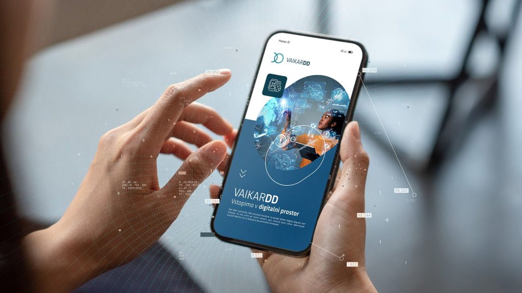 Ženske roke držijo v rokah telefon, na zaslonu naslovna stran aplikacije VAIKARDD