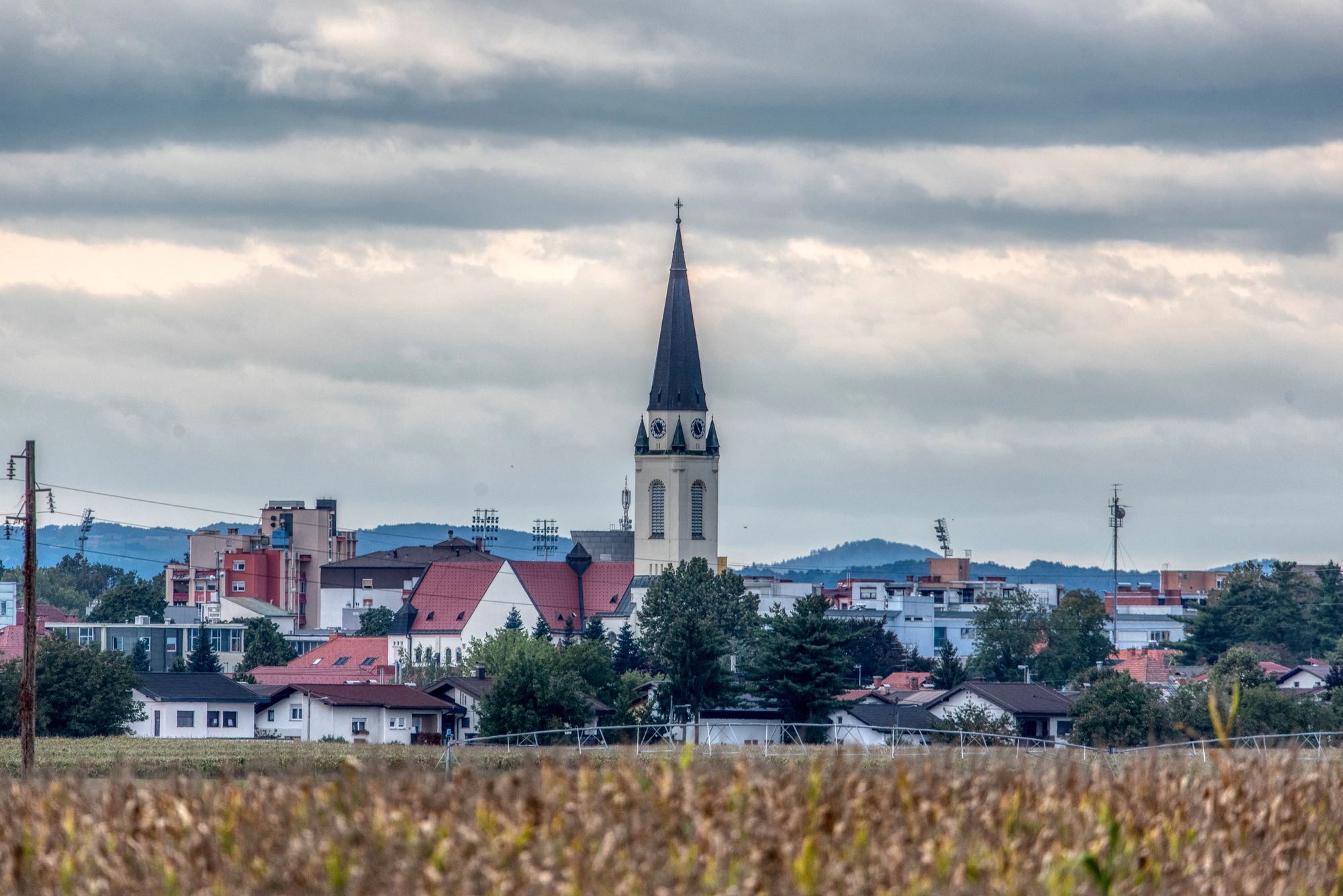 V ospredju njiva, v ozadju naselje cerkvijo v sredini.