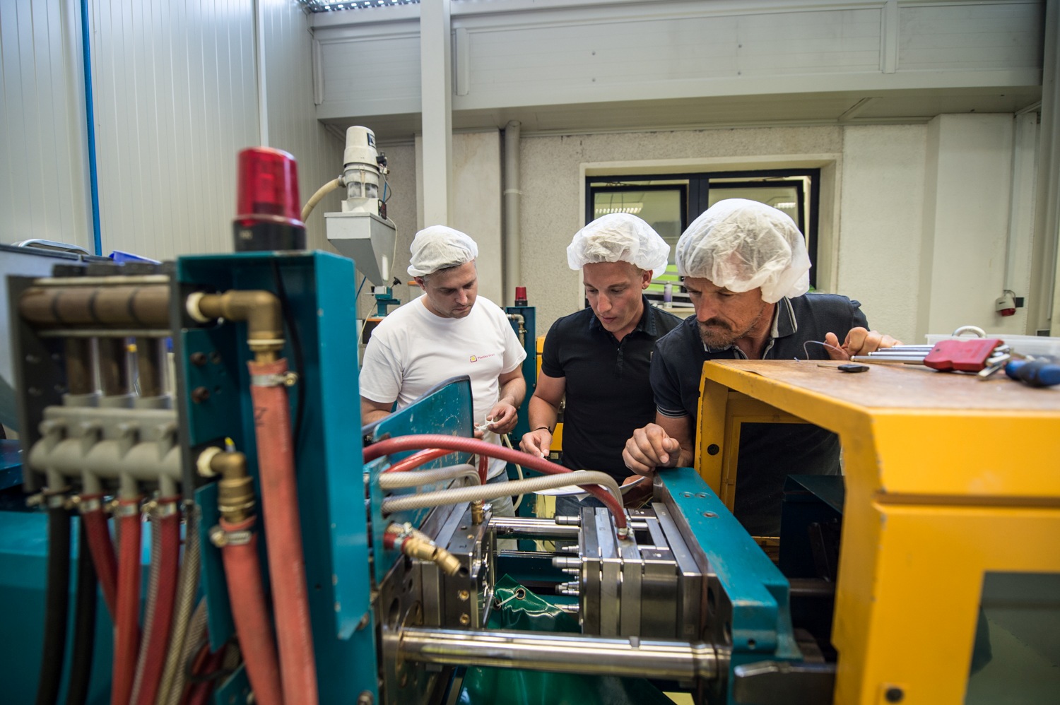 Trije delavci za strojem v proizvodnji.
