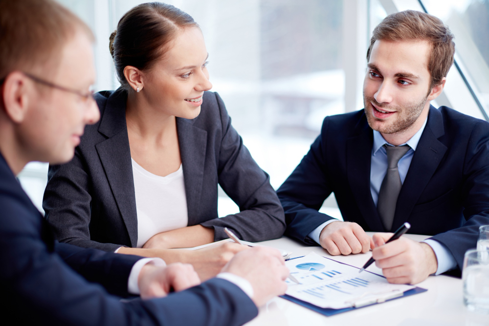 Dva mlada podjetnika in podjetnica sedijo za mizo med sestankom.